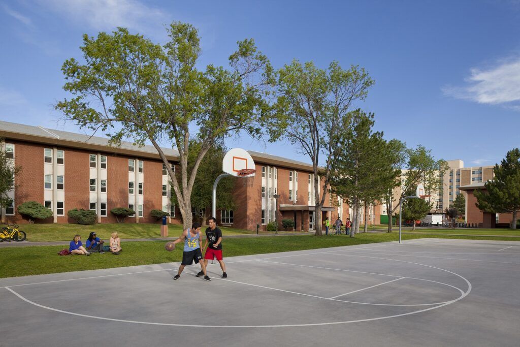 Two N A U students playing basketball on an outdoor court next to Allen Hall.