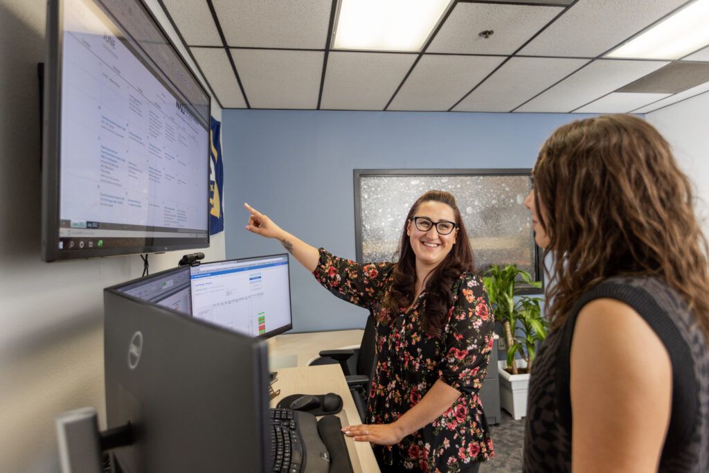 N A U staff and business intelligence analyst pointing at a screen and working with a coworker.