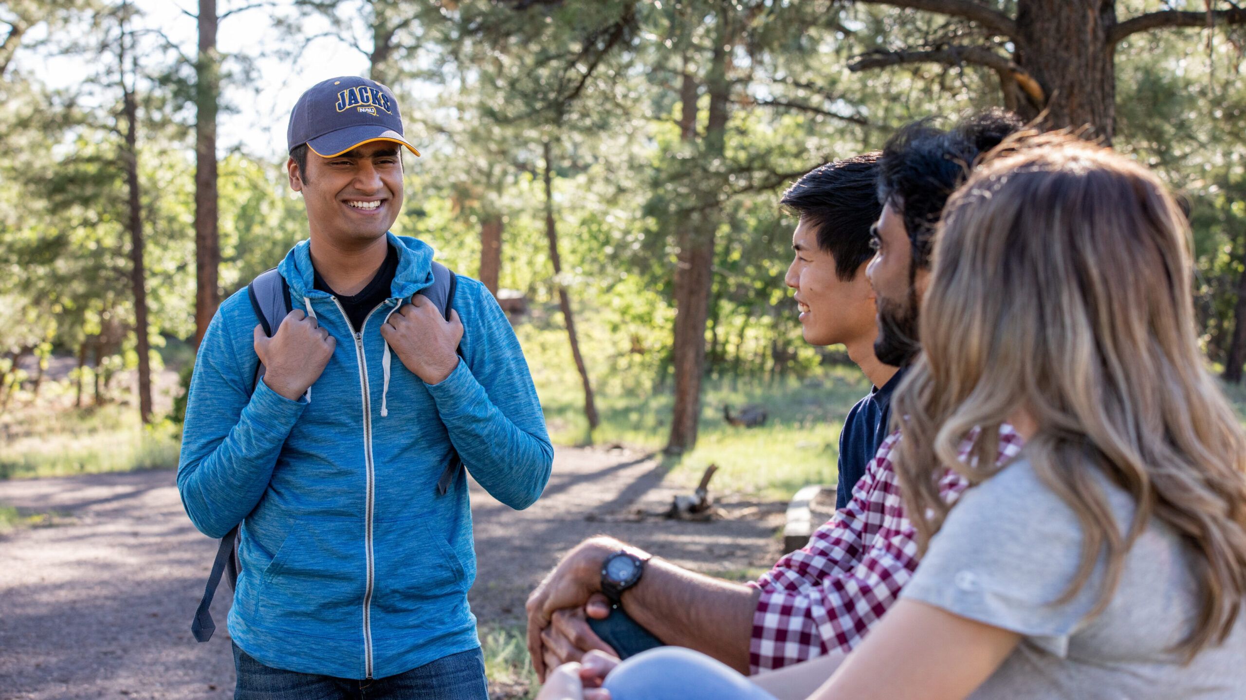 Four NAU students pause during a hike to take a break and chat with each other on a scenic outdoor trail.