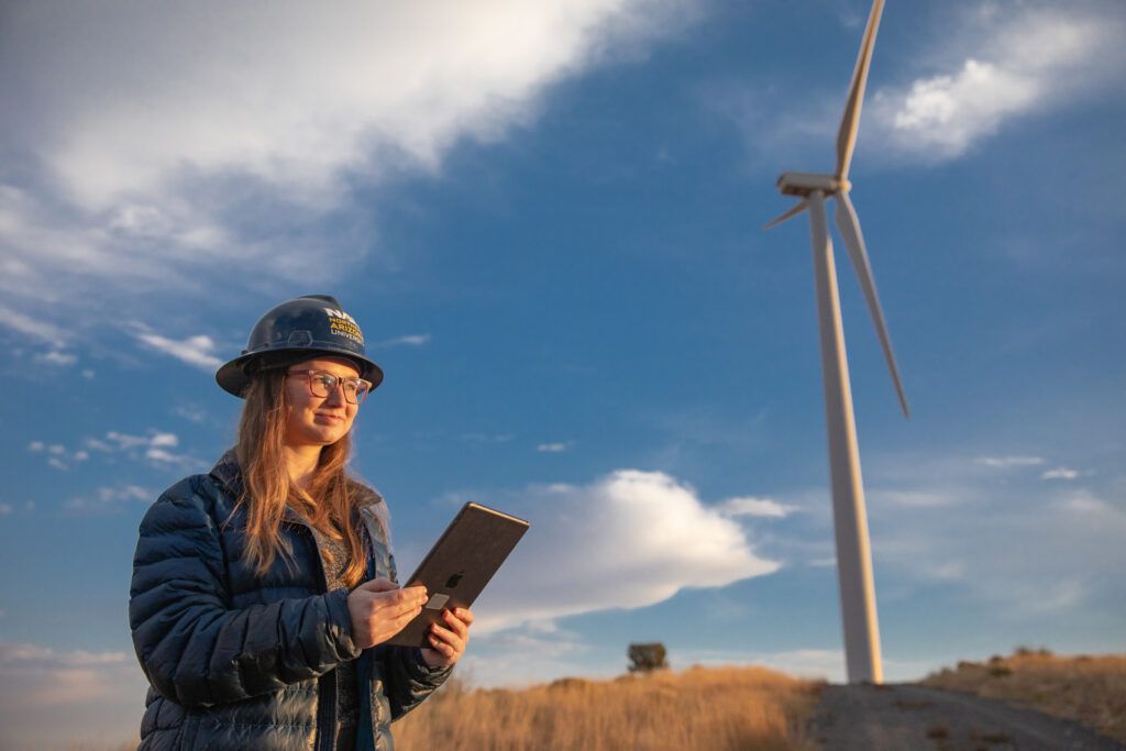 An N A U student works on her tablet at a wind farm near a turbine.