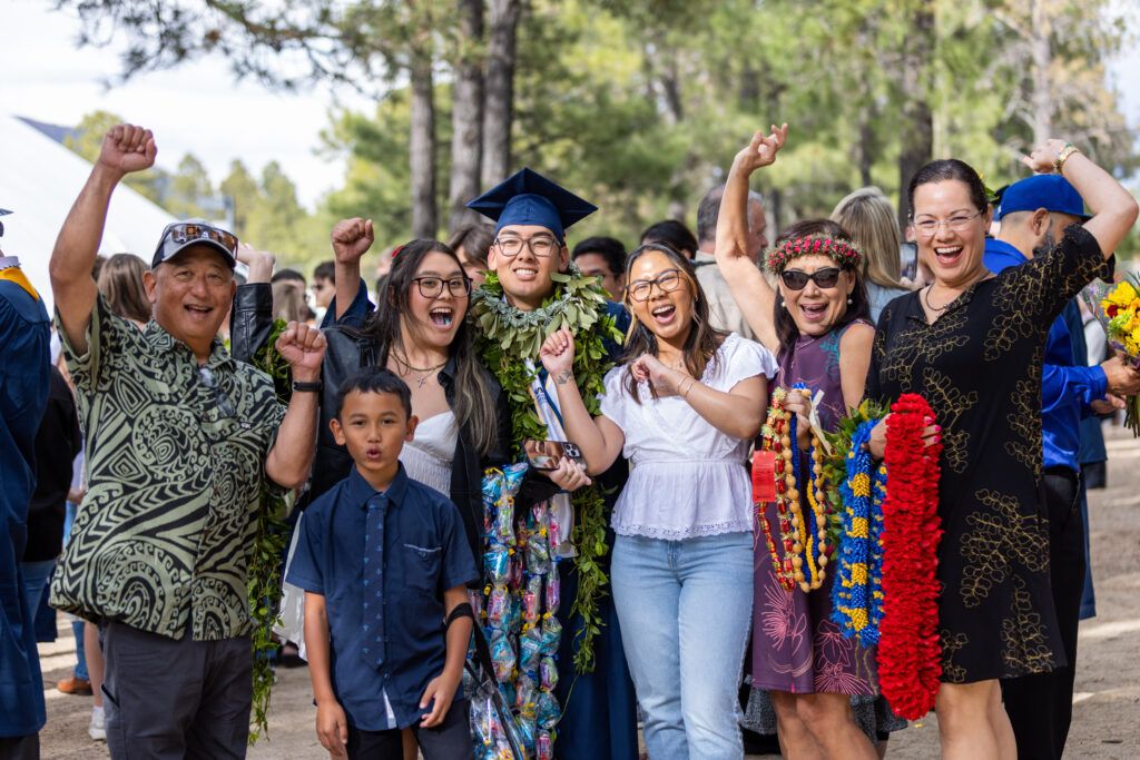 An N A U student and their family cheer happily while posing at commencement.