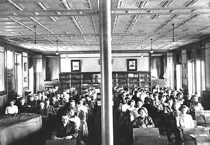 A black and white photograph captured in 1911 of students sitting in the original Old Main classroom.