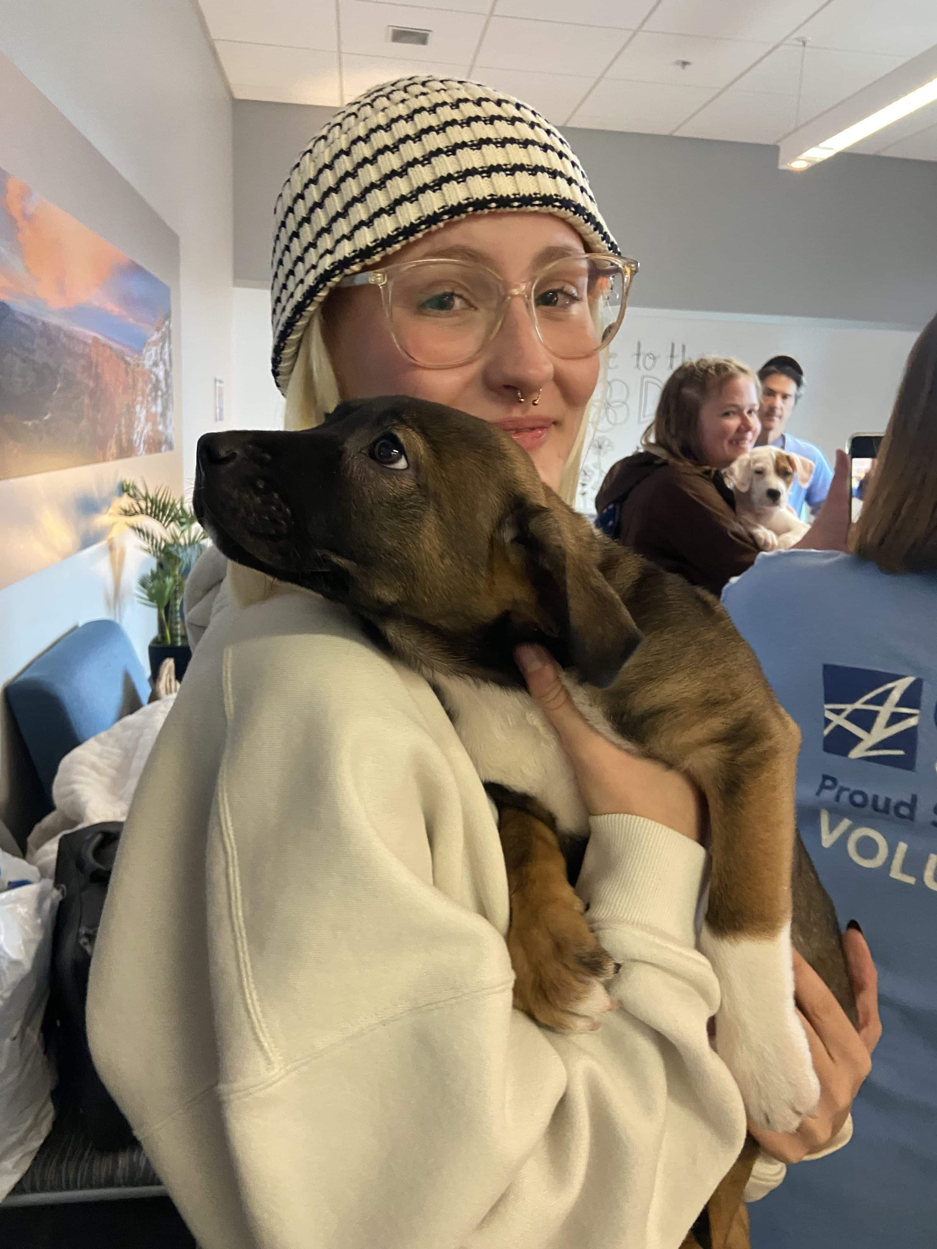 A student in a black-and-white knitted hat holds a brown puppy in her arms.