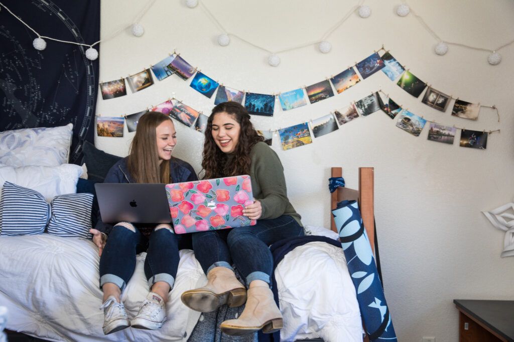 Two students work on their laptops in a dorm room.