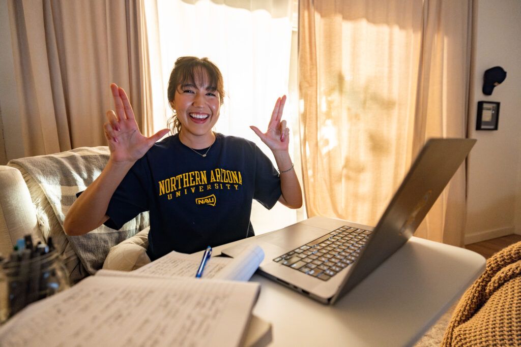 An N A U Online student does the Lumberjack hand symbol while happily working from home.