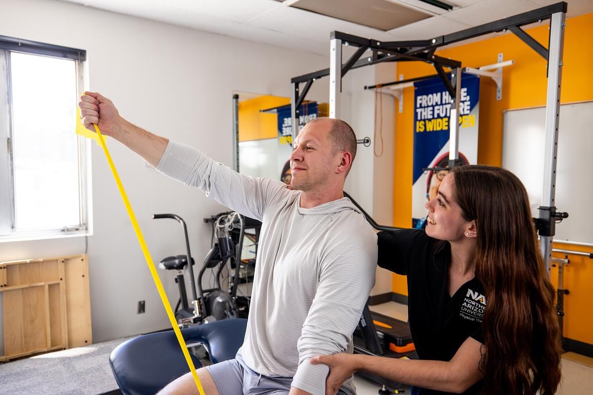 A physical therapy student helps a patient with an exercise band stretch.