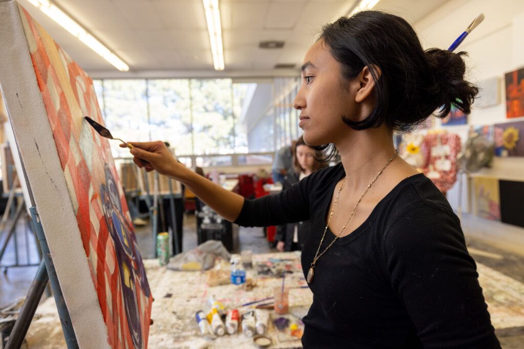 An N A U student uses a palette knife to apply paint on canvas.