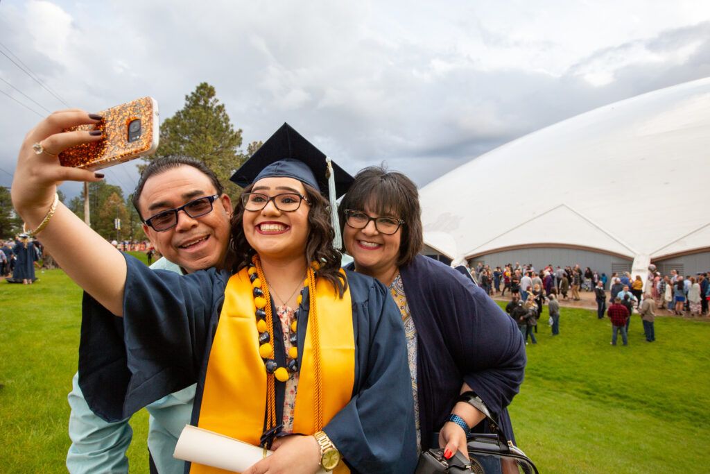 An N A U graduate smiles while posing with their parents at commencement.