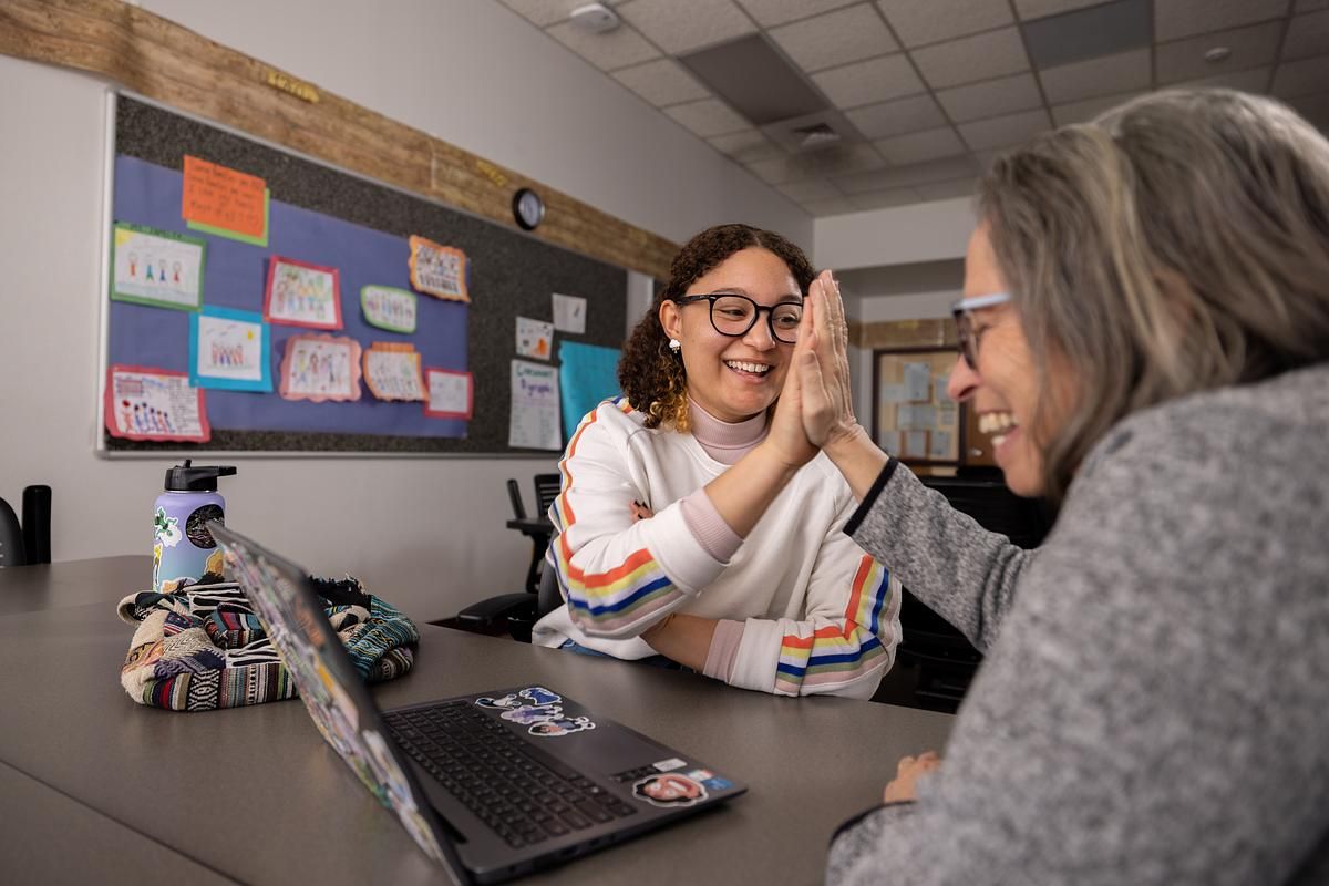 A student and professor look at a laptop and high-five.
