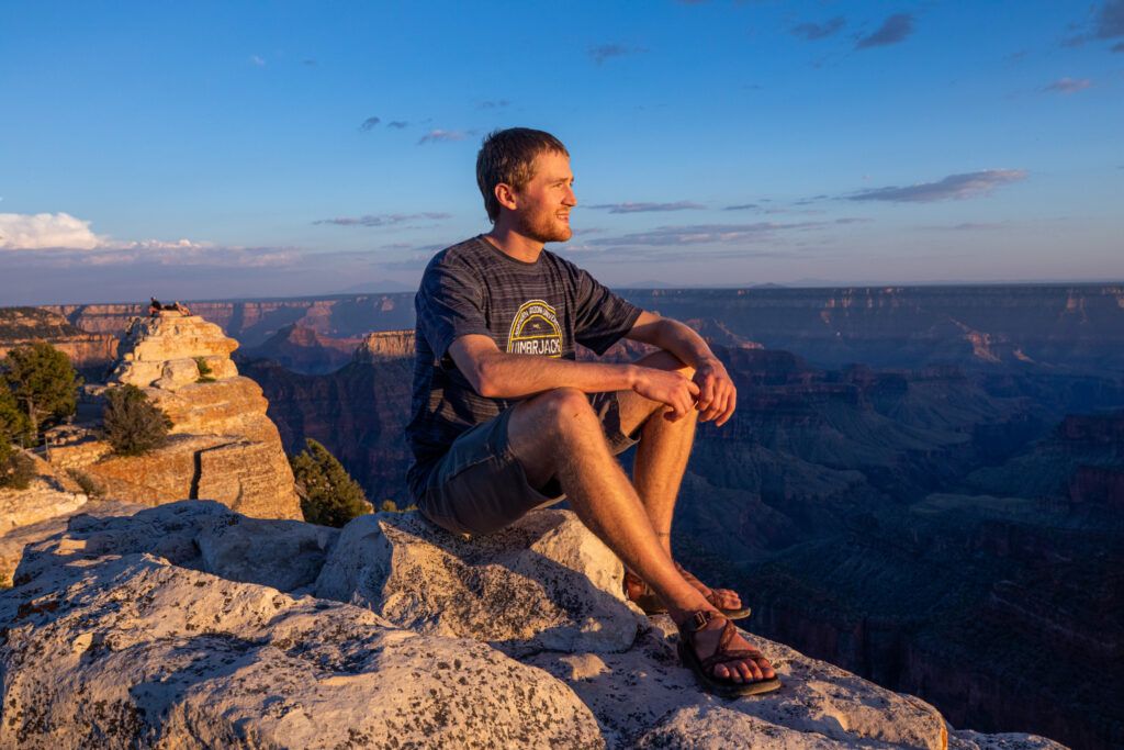 A student wearing an N A U shirt watches the sun set at the Grand Canyon National Park.