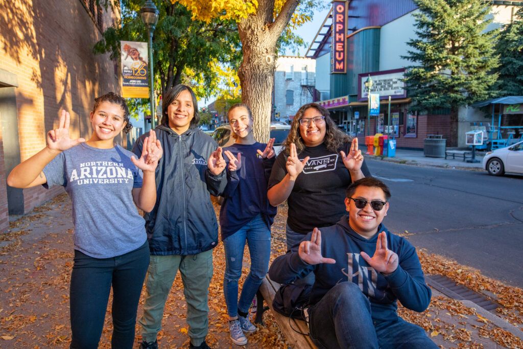 A group of N A U students hang out in downtown Flagstaff, posing for a picture with L J's hand signs.