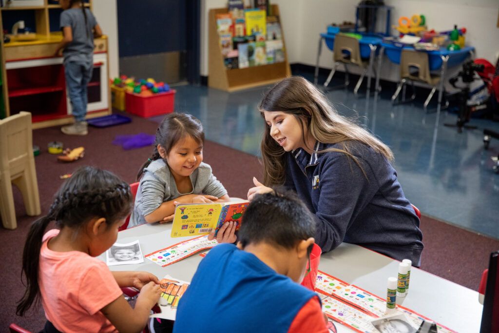 A teacher reads to young students in class while they work on an arts project.