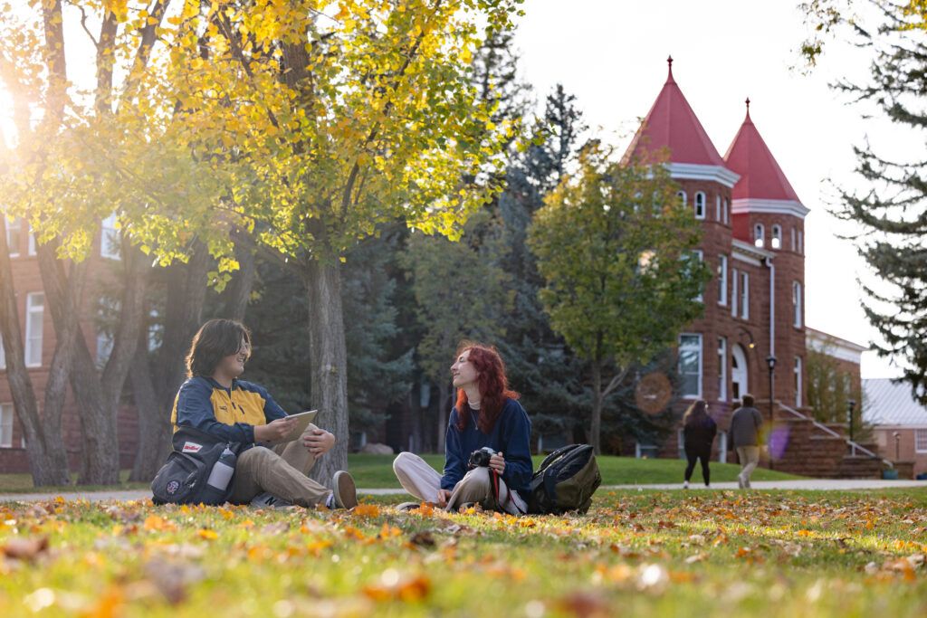 Two students chat on the lawn in-front of old main in the fall.